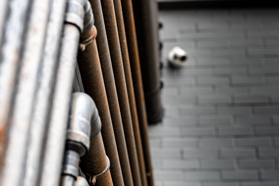 Close-up of rusted metal pipes running vertically along a gray brick wall with a security camera mounted in the background.