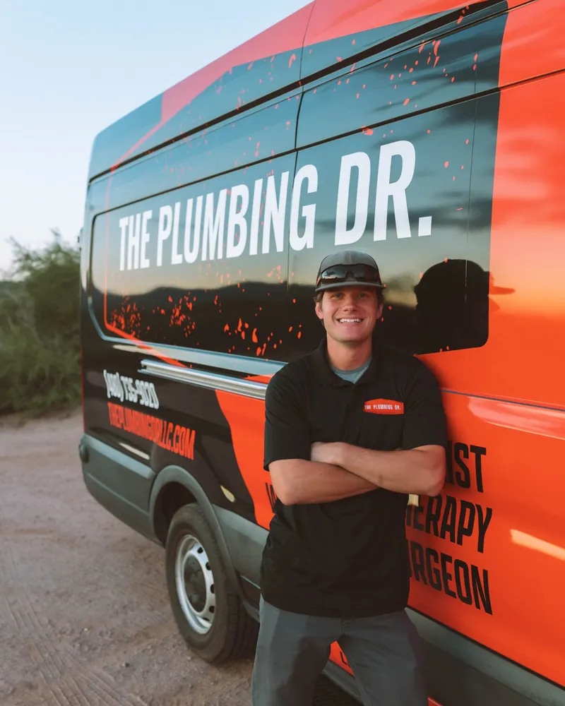 Ryan, plumbing technician at The Plumbing Dr., arms crossed in front of a company service van