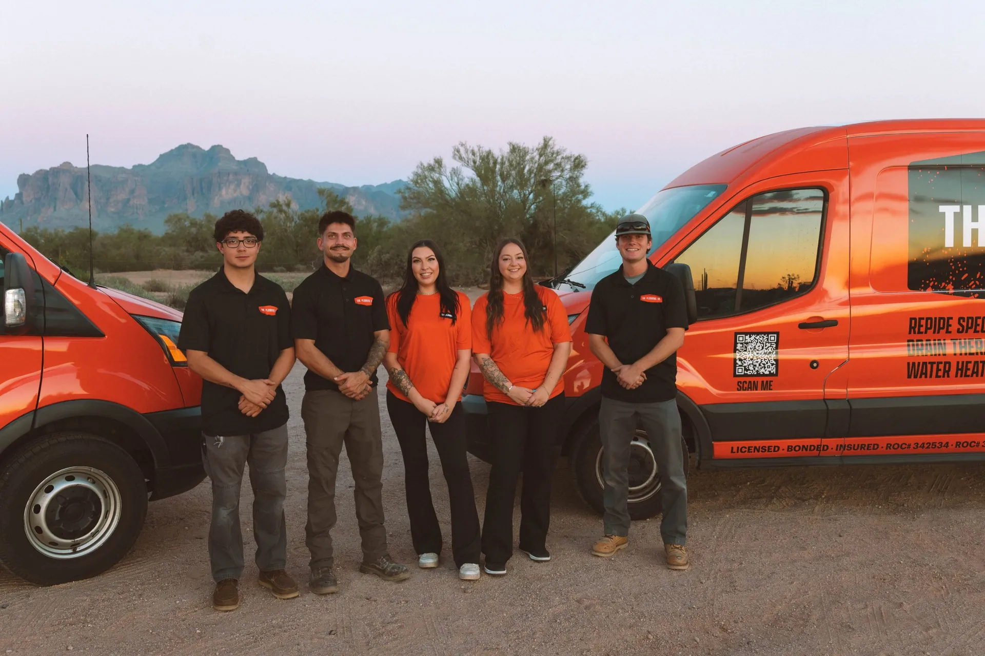 The Plumbing Dr. team standing between two company service vans with the Superstition Mountains behind them
