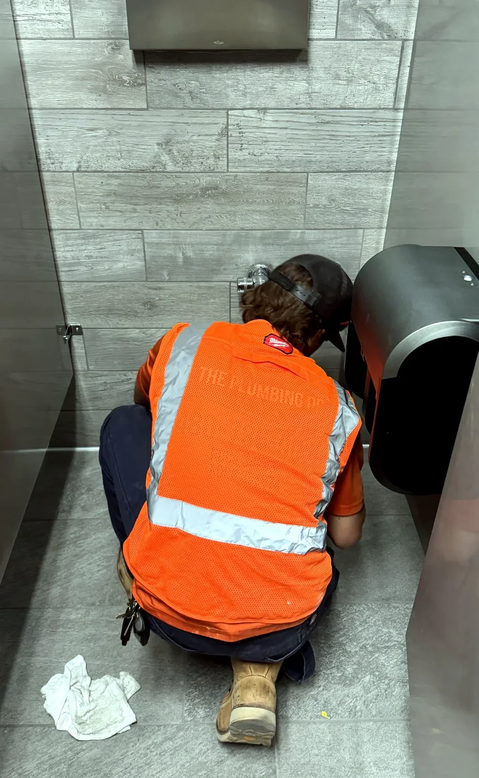 The Plumbing Dr. technician in a hi-vis vest servicing a commercial restroom fixture