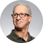 Middle-aged man with gray hair and glasses wearing a dark polo shirt, looking slightly to the side.