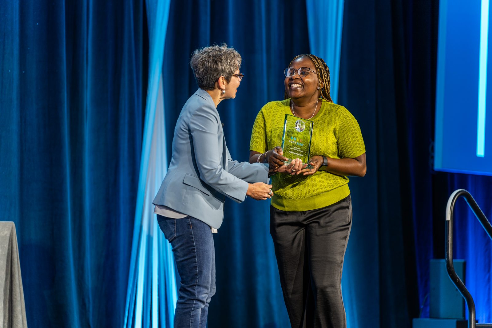A Next Gen Leadership Award recipient is handed her award on stage at an AGBT meeting.