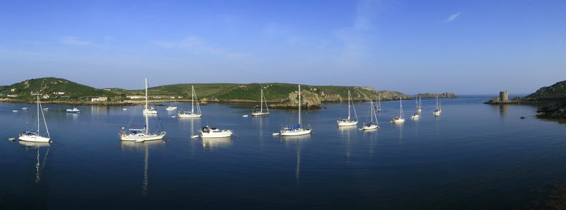 A sailboat moored in a sheltered cove with rocky islands beyond