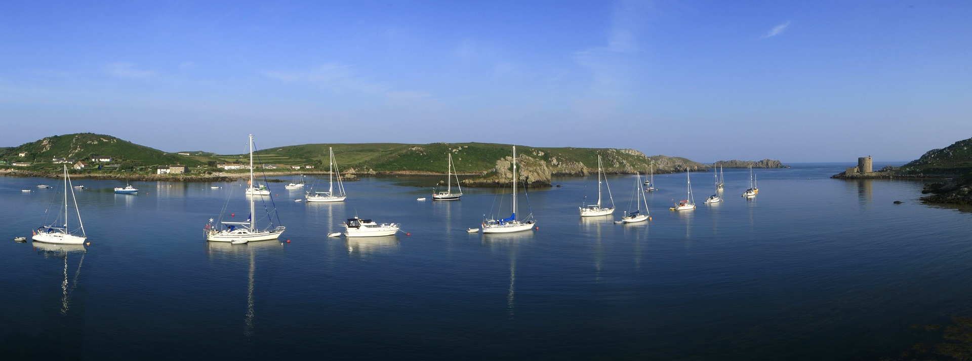 A sailboat moored in a sheltered cove with rocky islands beyond