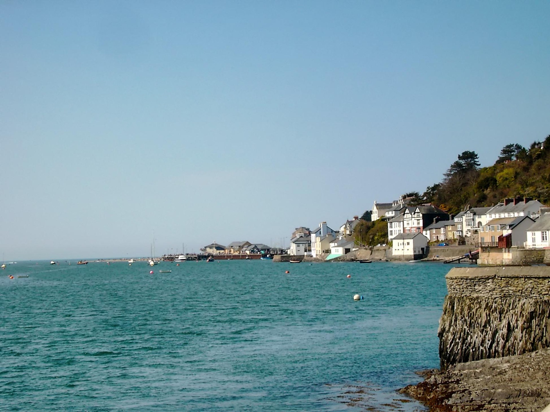A harbor town at low tide with boats resting on the sand beneath a hillside