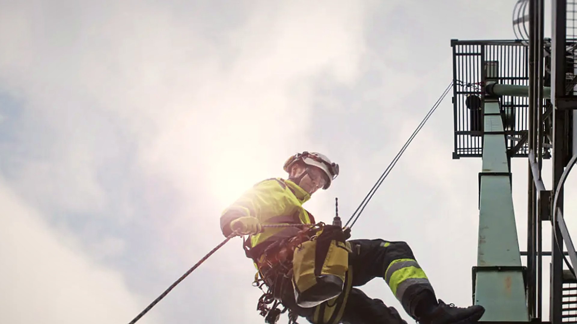 Worker in harness and helmet abseiling from a steel tower