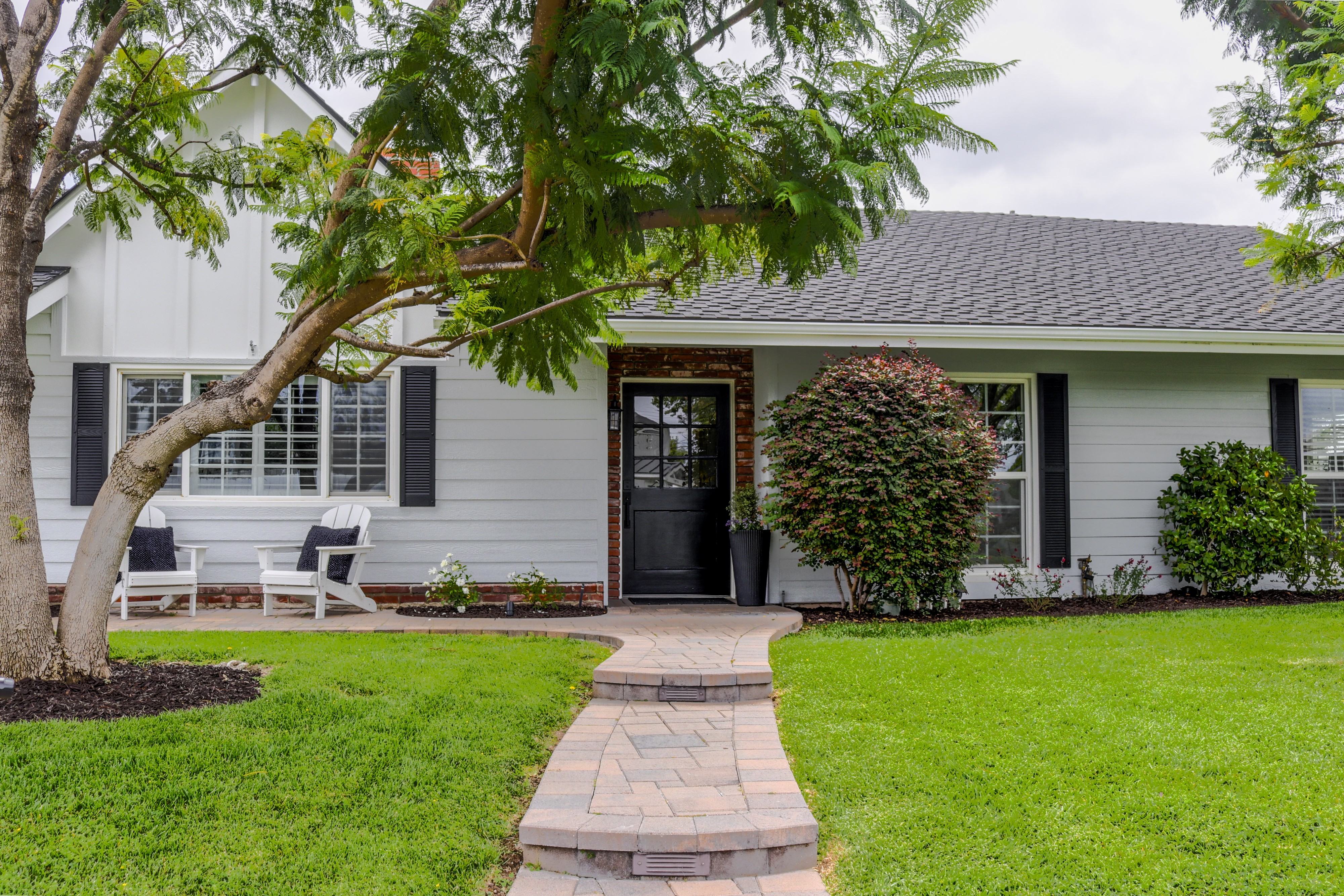 Front entry with dark door and brick walkway framed by a mature shade tree, Tustin home for sale