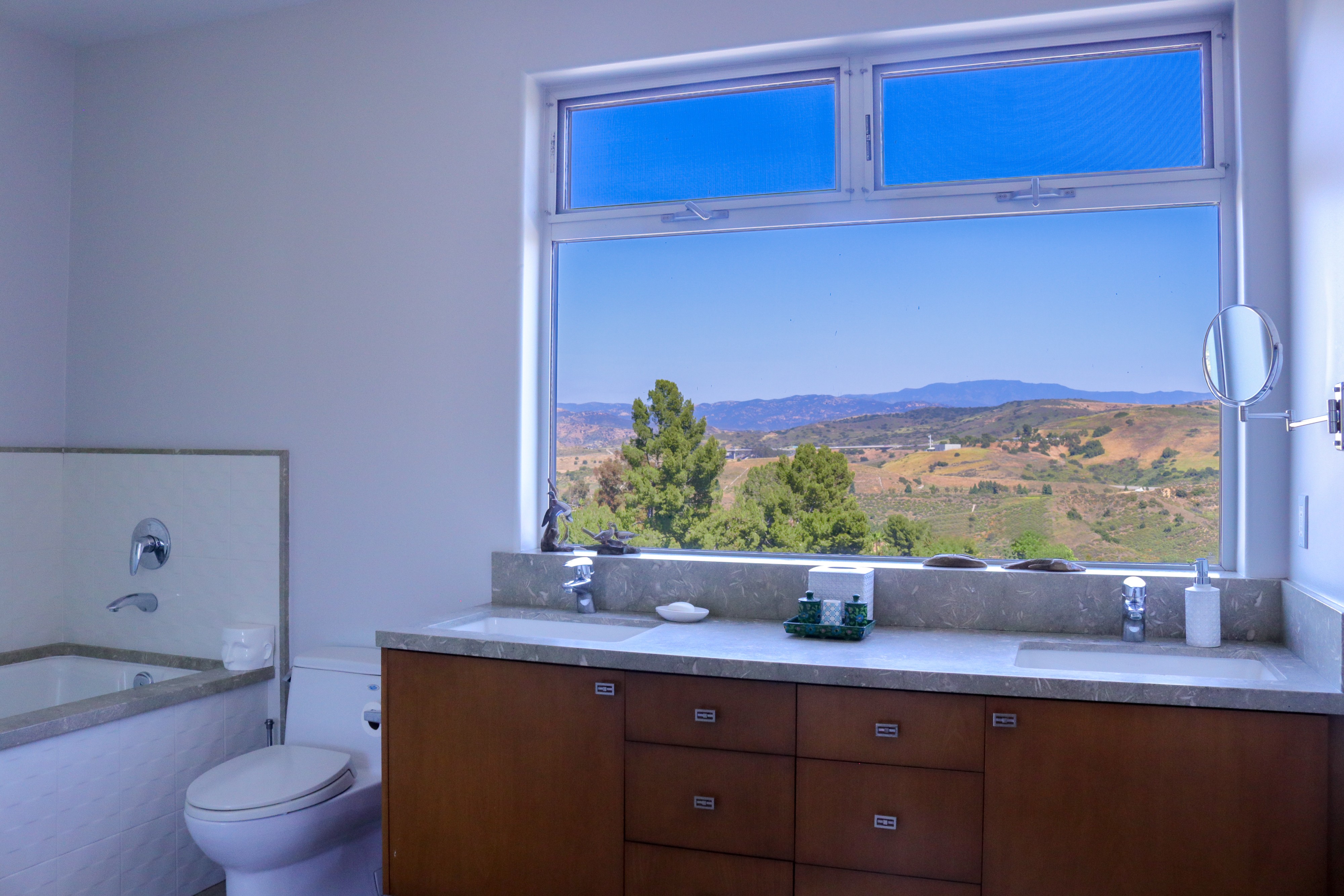 Bathroom with double vanity beneath a wide window and hillside view, Tustin home