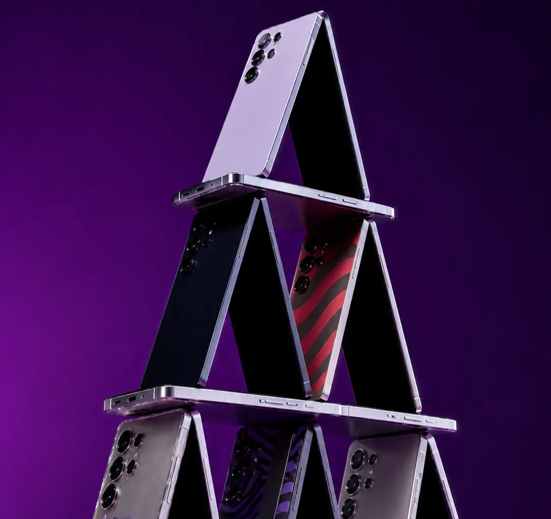 Smartphones balanced into a pyramid against a purple backdrop