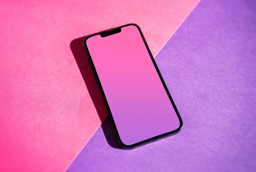 A smartphone resting on a pink and purple paper backdrop