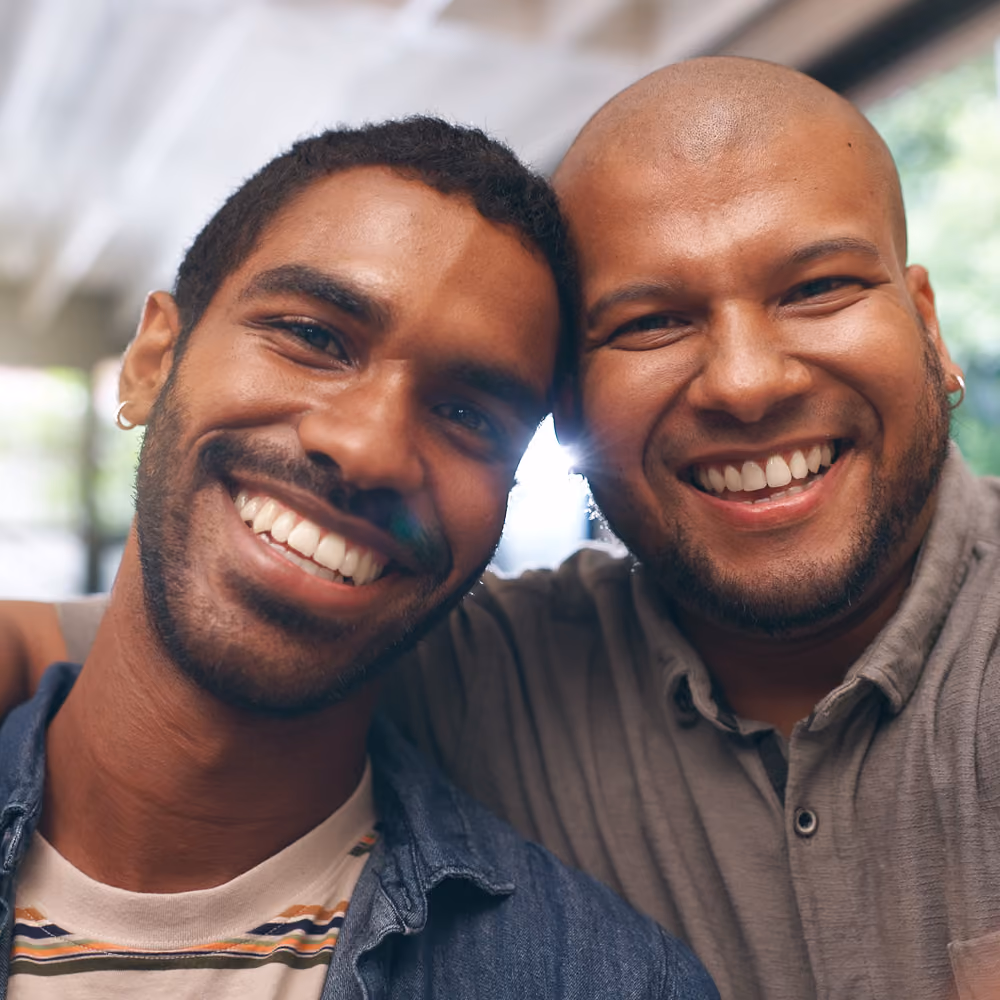 Two smiling men with their heads close together posing for a friendly close-up photo.