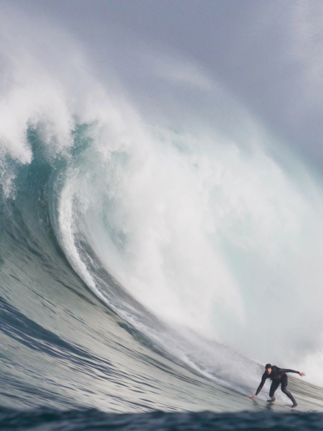 Matt Bromley racing down a huge blue wave as it breaks behind him