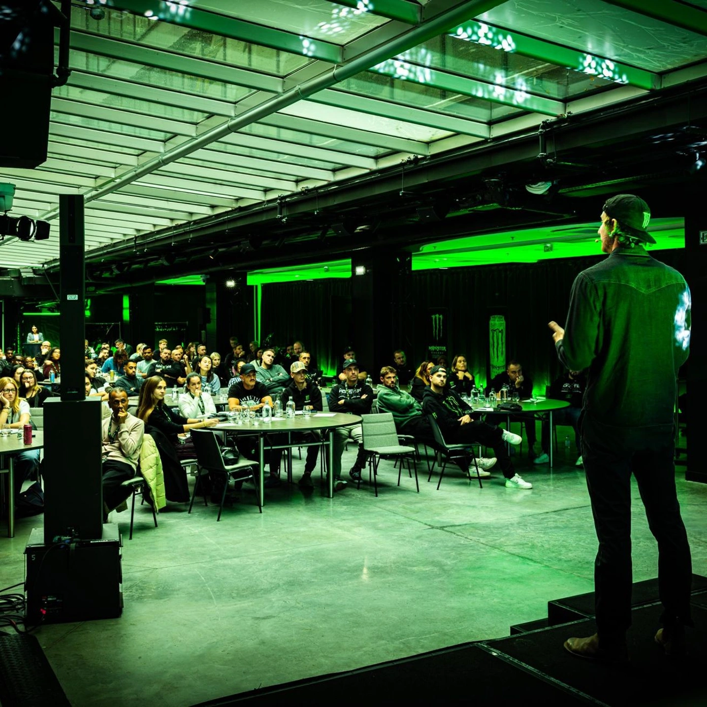 Matt Bromley on stage presenting to a seated audience under green stage lighting