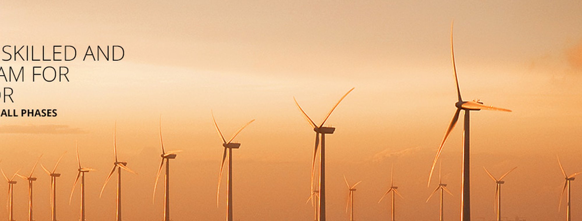 A row of wind turbines standing tall against a warm, orange sky at sunset or sunrise.