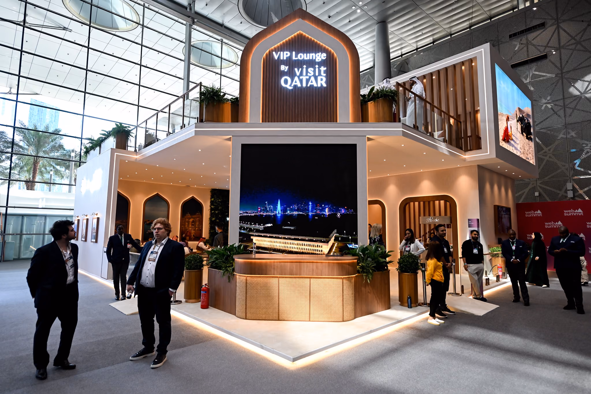 The front of the VIP lounge, with attendees in business attire stopping nearby. The entrance has a sign that reads VIP Lounge by Visit Qatar
