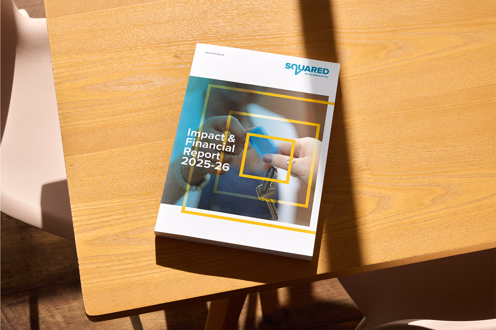 A booklet titled 'Impact & Financial Report 2025-26' with the SQUARED logo on the top right corner, placed on a wooden table with sunlight casting shadows.