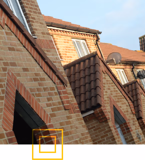 Close-up view of brick residential buildings with brown tiled roofs and white-framed windows under a clear sky.