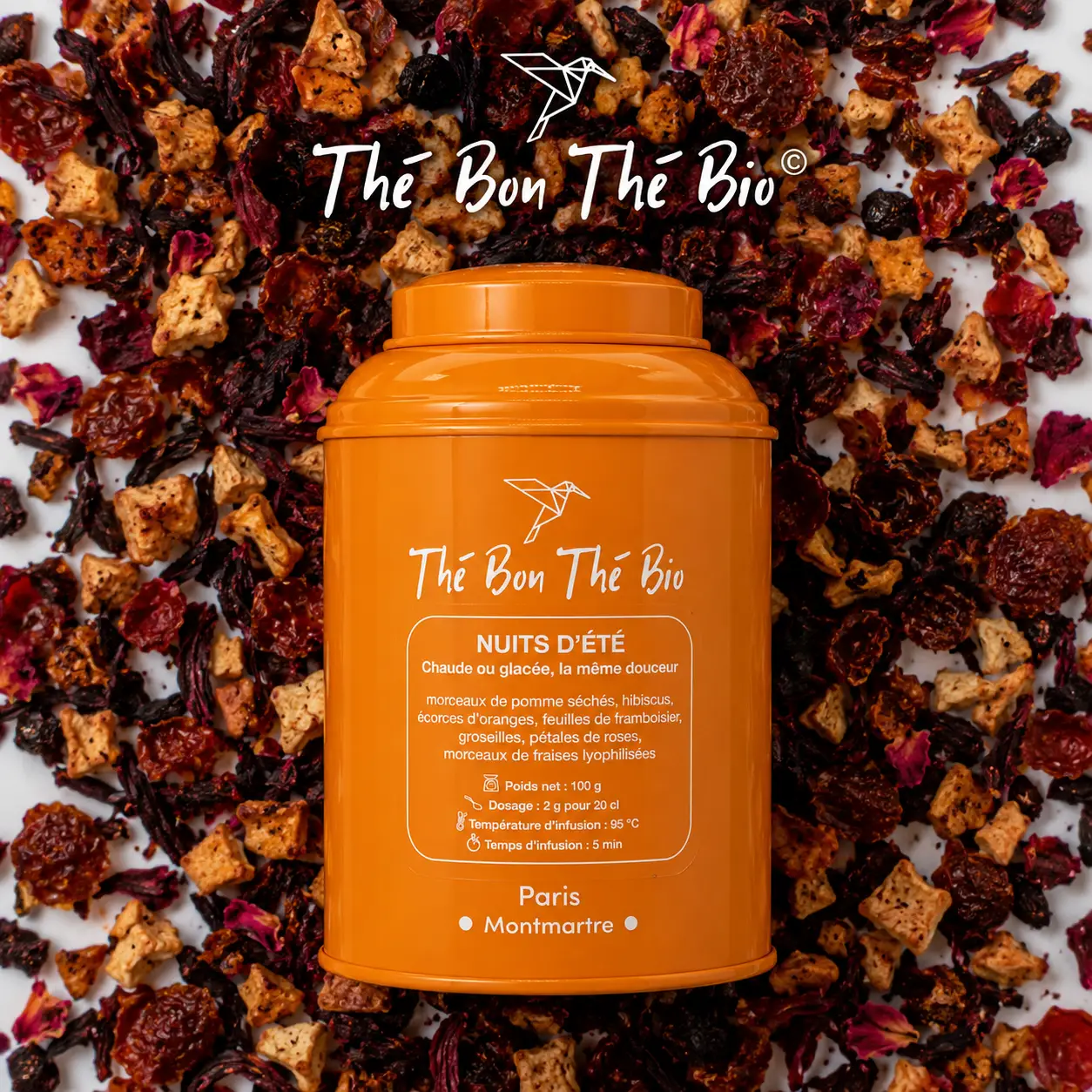 Boîte orange de thé bio Thé Bon Thé Bio Nuits d'été, entourée de morceaux colorés de thé aux fruits séchés et fleurs, sur fond blanc.