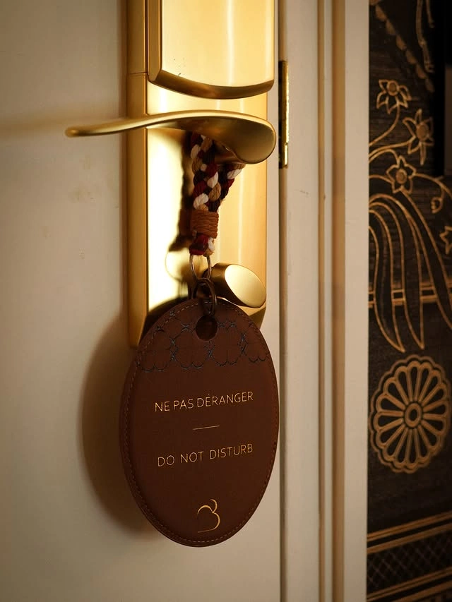 Panneau "Ne pas déranger" en cuir marron accroché à une poignée de porte dorée avec une corde tressée multicolore.