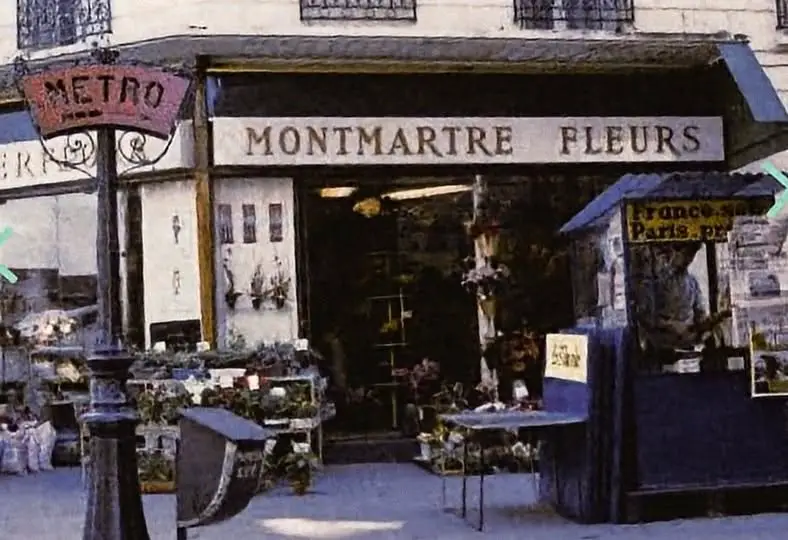 Façade d'une boutique de fleurs nommée Montmartre Fleurs avec des plantes exposées devant et un panneau du métro parisien à proximité.