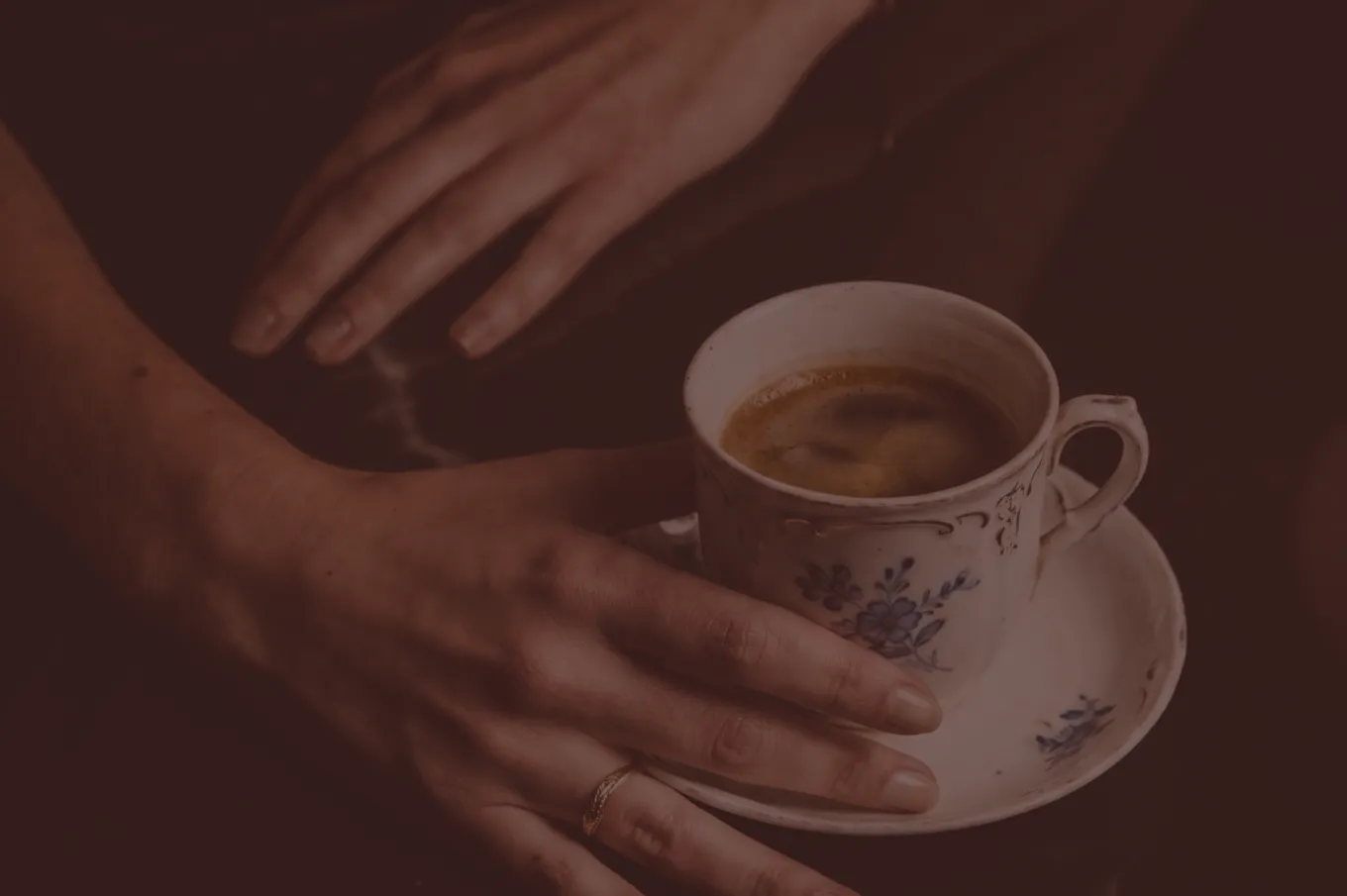 Main délicate tenant une tasse de café fumant avec soucoupe décorée de fleurs bleues.