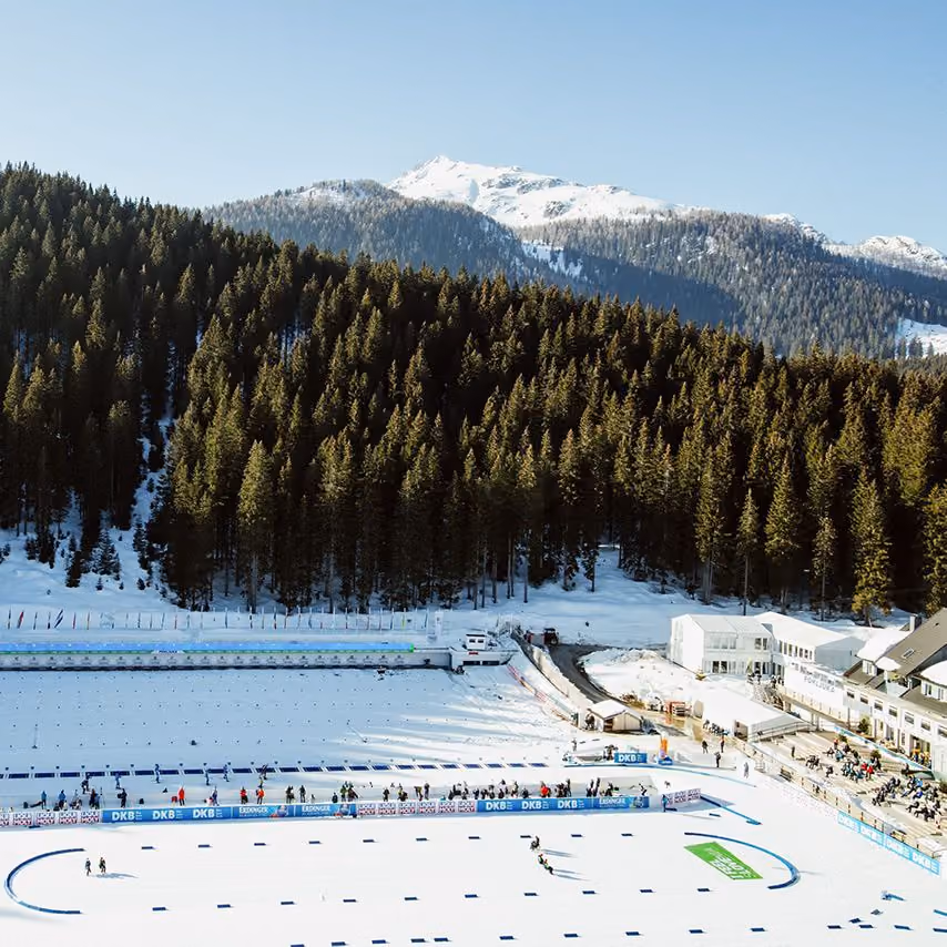 Biatlonski stadion s zasneženo progo in strelišči, v ozadju gozd in zasneženi vrhovi