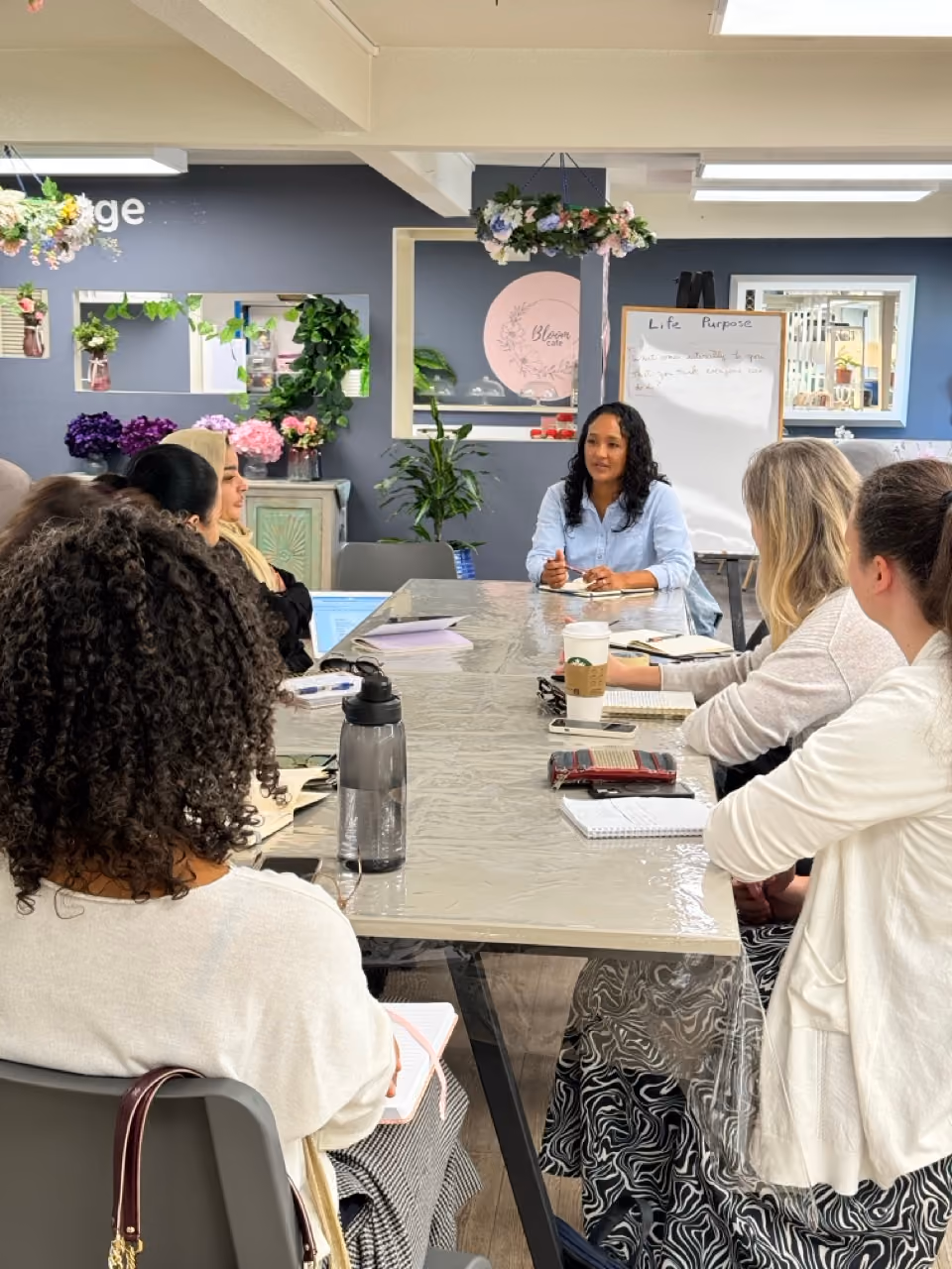 A group of six women seated around a conference table engaged in a discussion with Clementine at the head of the table who is speaking and gesturing.