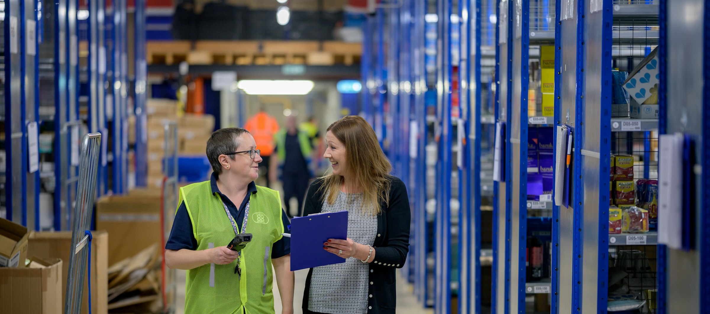 Deux collègues échangent en souriant dans les allées d'un entrepôt logistique