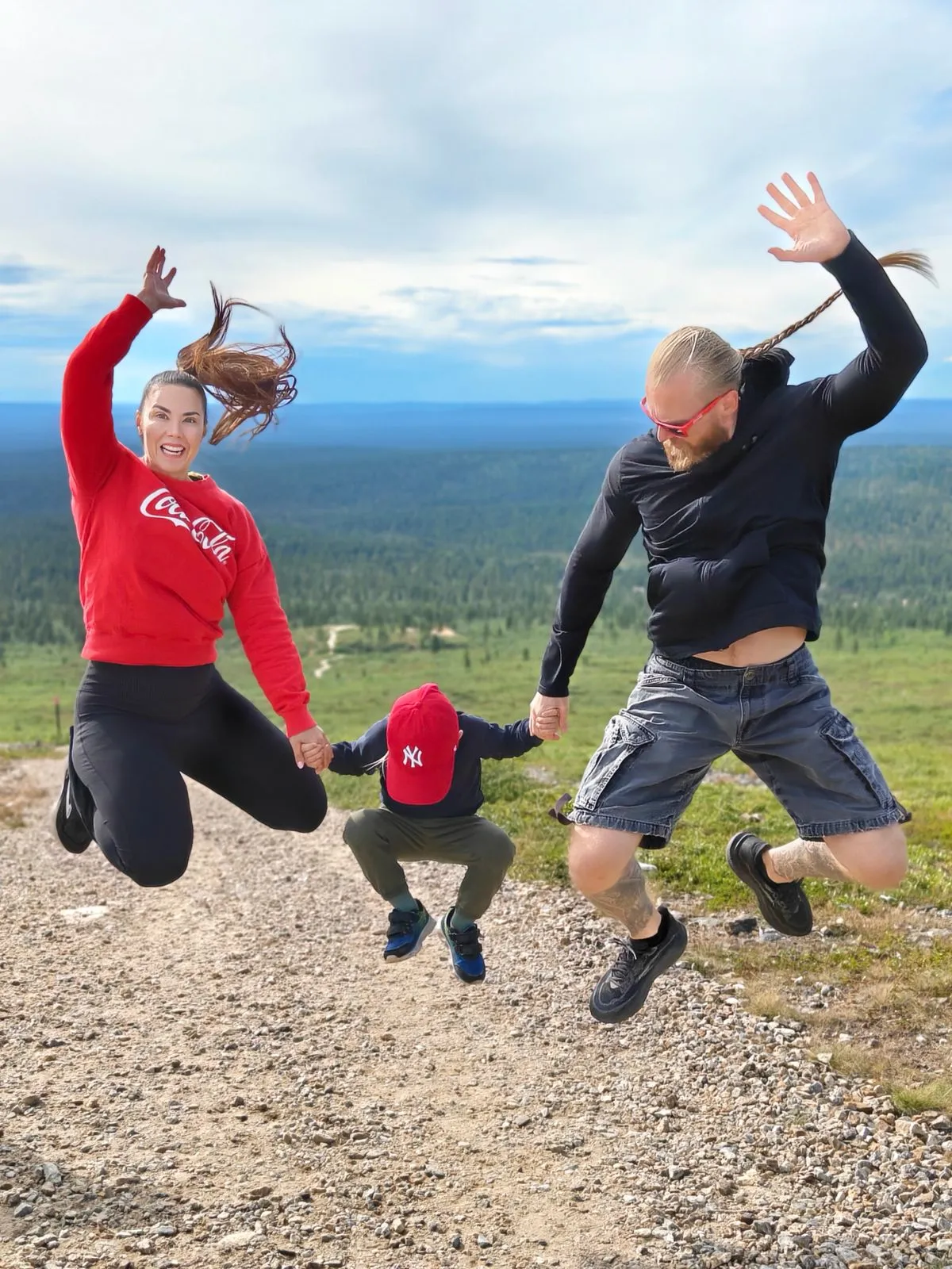 Perhe hyppää yhdessä ulkona luonnossa harjoittaen voimavalmennusta ja liikkuvuutta.
