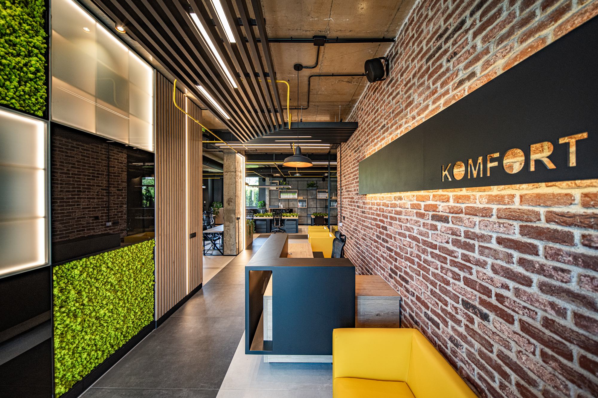 Comfort Partners Headquarters — the Komfort sign in black metal on the brick wall, moss panels opposite