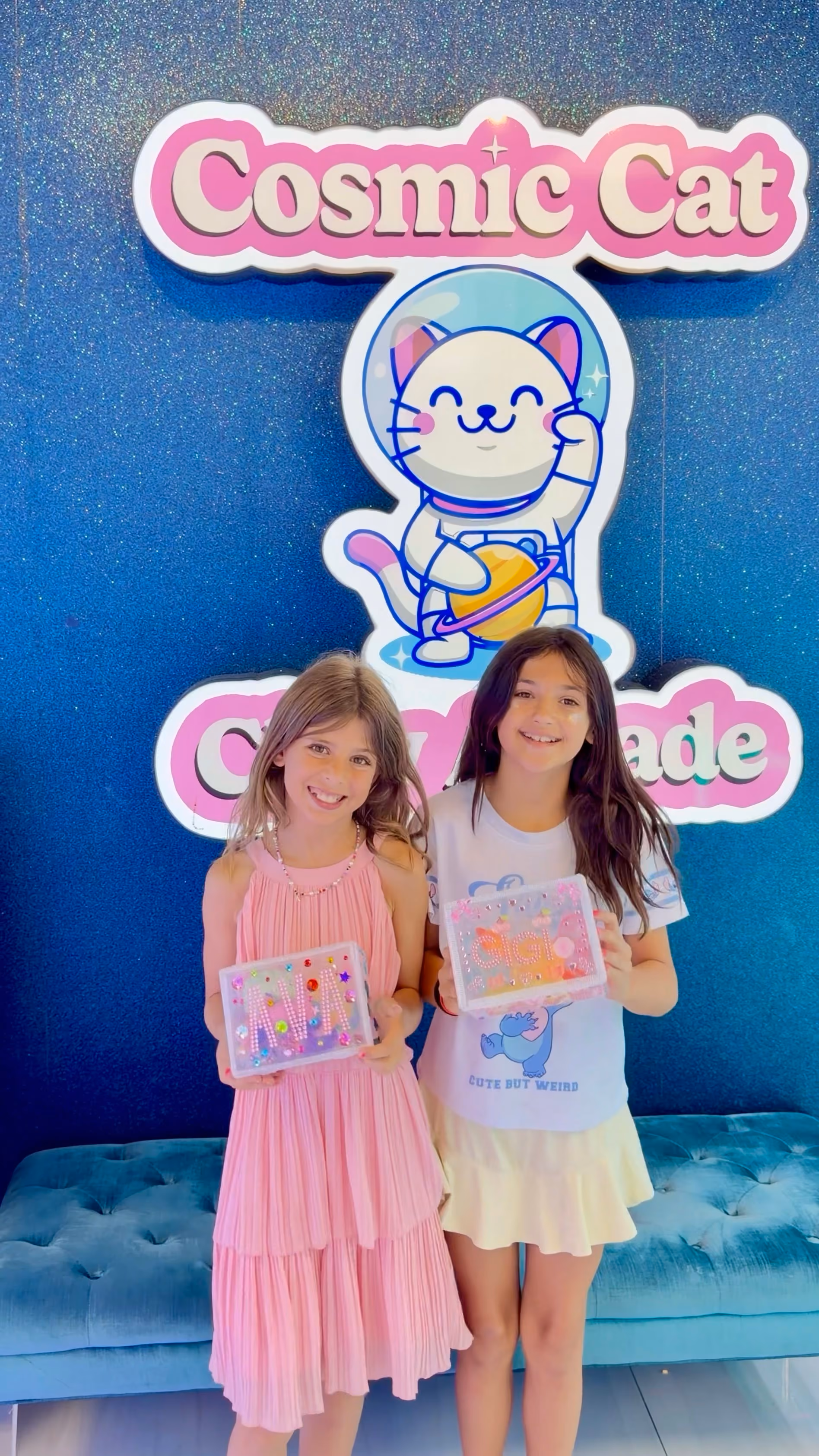 Two girls under the Cosmic Cat sign holding the keepsake boxes they decorated