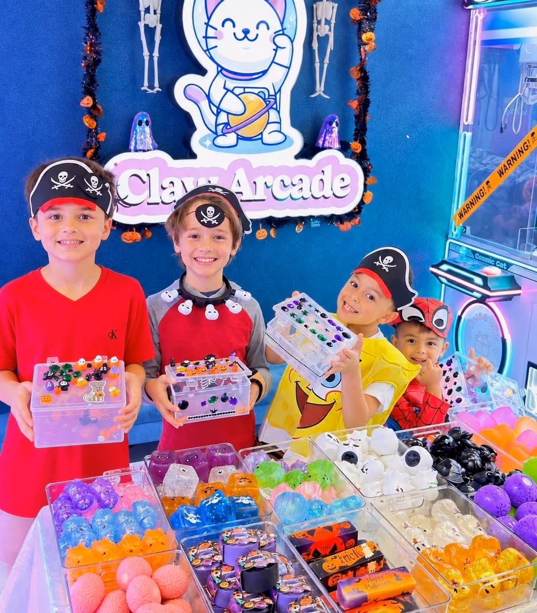 Four boys in pirate hats show off their decorated keepsake boxes behind trays of Halloween squishies