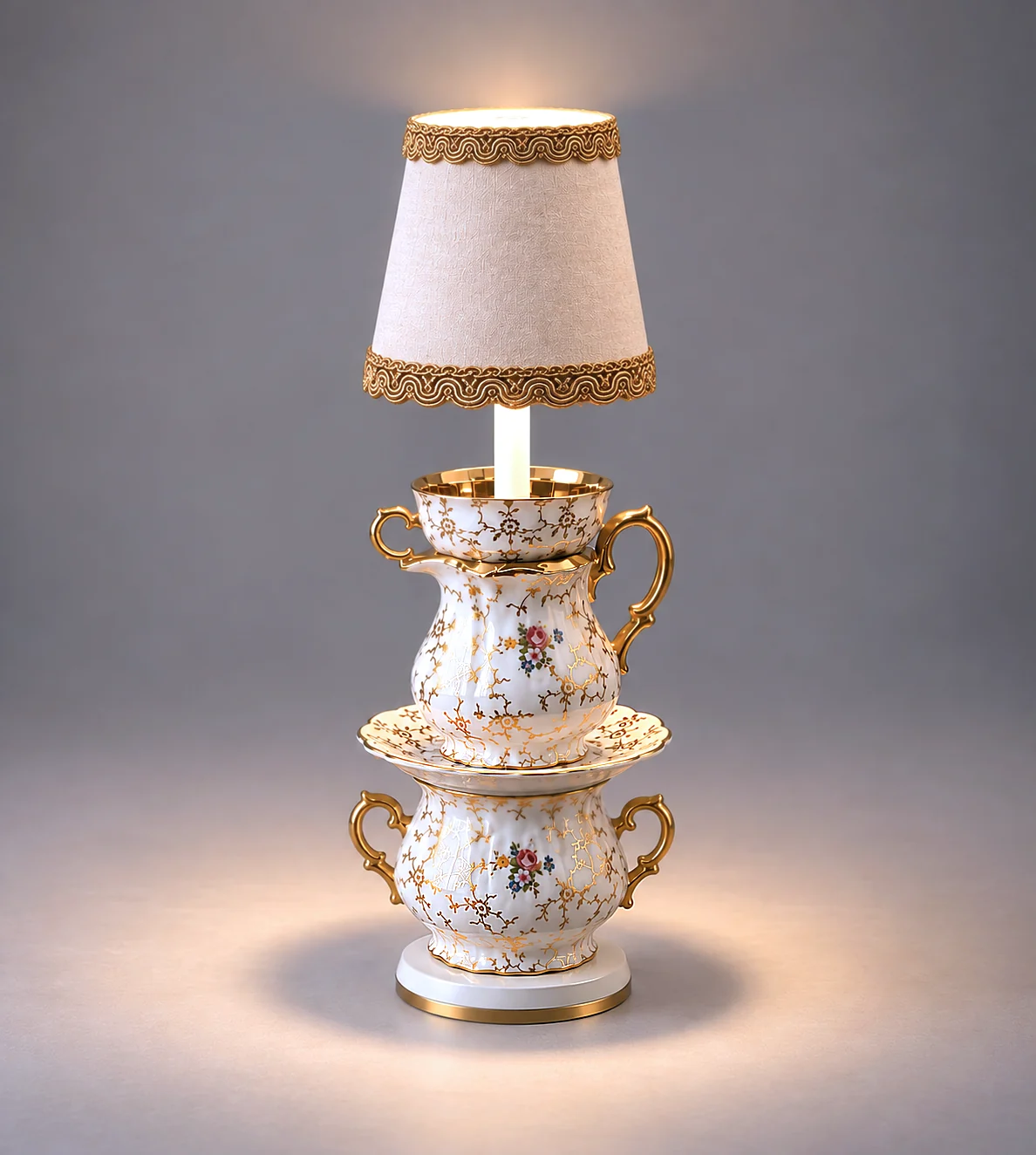 Vintage-style lamp made from stacked ornate porcelain teacups and plates with gold accents, topped with a cream-colored fabric lampshade with lace trim, sitting on a wooden table with warm lighting.