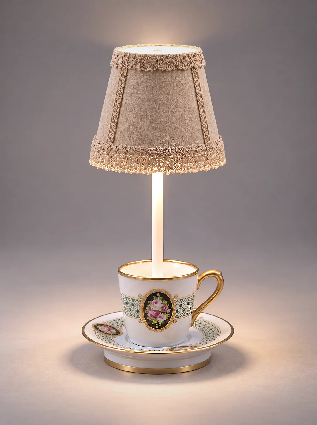 Vintage porcelain teapot with floral and gold details converted into a table lamp with a small lace-trimmed beige lampshade and matching teacup on top, set on a restaurant table with a wine glass and folded napkin nearby.