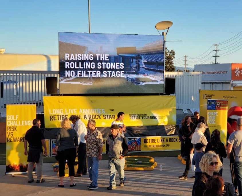 A large group of people are standing in front of a large screen with the words