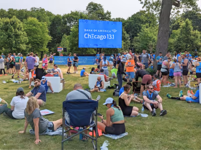 Runners resting on grass near a Bank of America Chicago 13.1 event banner in a park setting.
