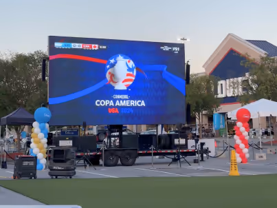 Outdoor screen showing Copa America soccer event with red, white, and blue balloon columns nearby.