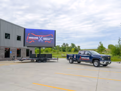 Pickup truck and trailer with digital signage displaying Insane Impact branding near a building.