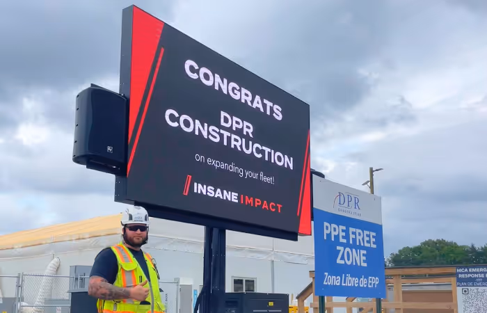 Construction worker standing next to a sign congratulating DPR Construction on fleet expansion.