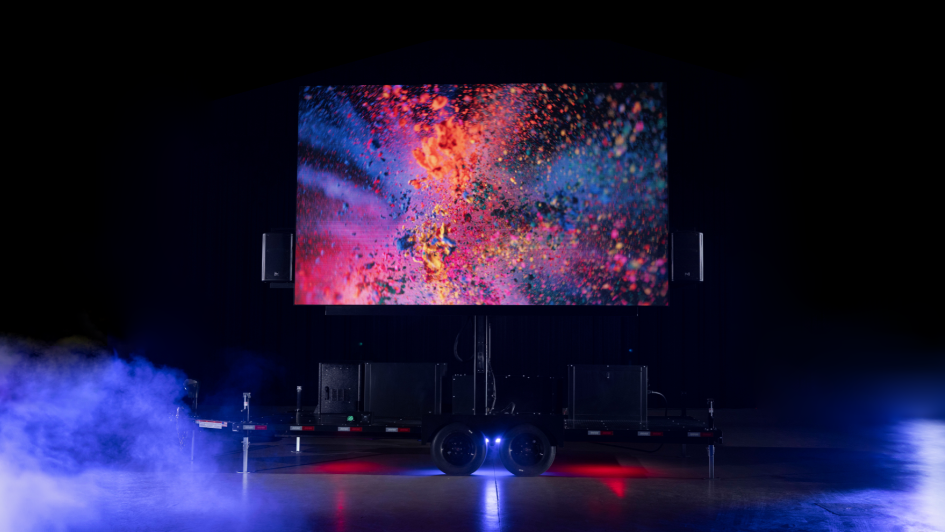 Large outdoor digital screen on trailer showing colorful abstract explosion with mist on the floor.