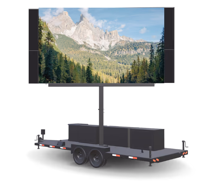 Large outdoor LED screen on trailer displaying mountain scene with trees under blue sky.
