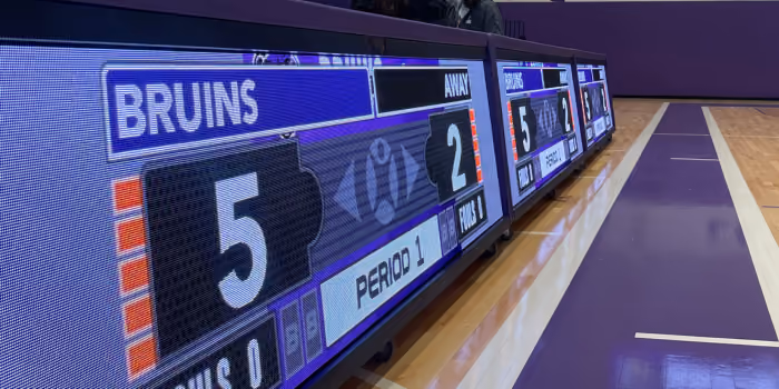 Electronic scoreboard showing Bruins leading 5 to 2 in period 1 on a gymnasium floor.