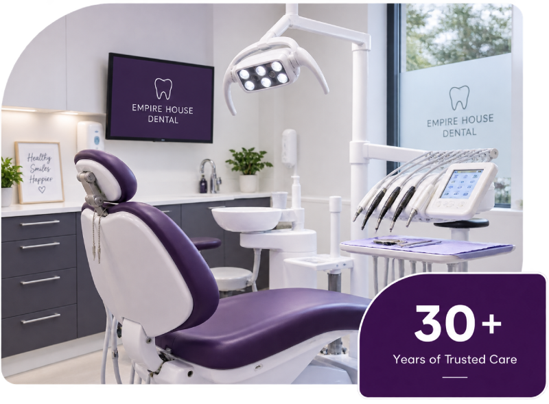 Modern dental clinic room featuring a purple and white dental chair with overhead light, dental instruments on a tray, and a screen displaying the Empire House Dental logo, with a sign that reads Healthy Smiles Happier and a label stating 30+ Years of Trusted Care.