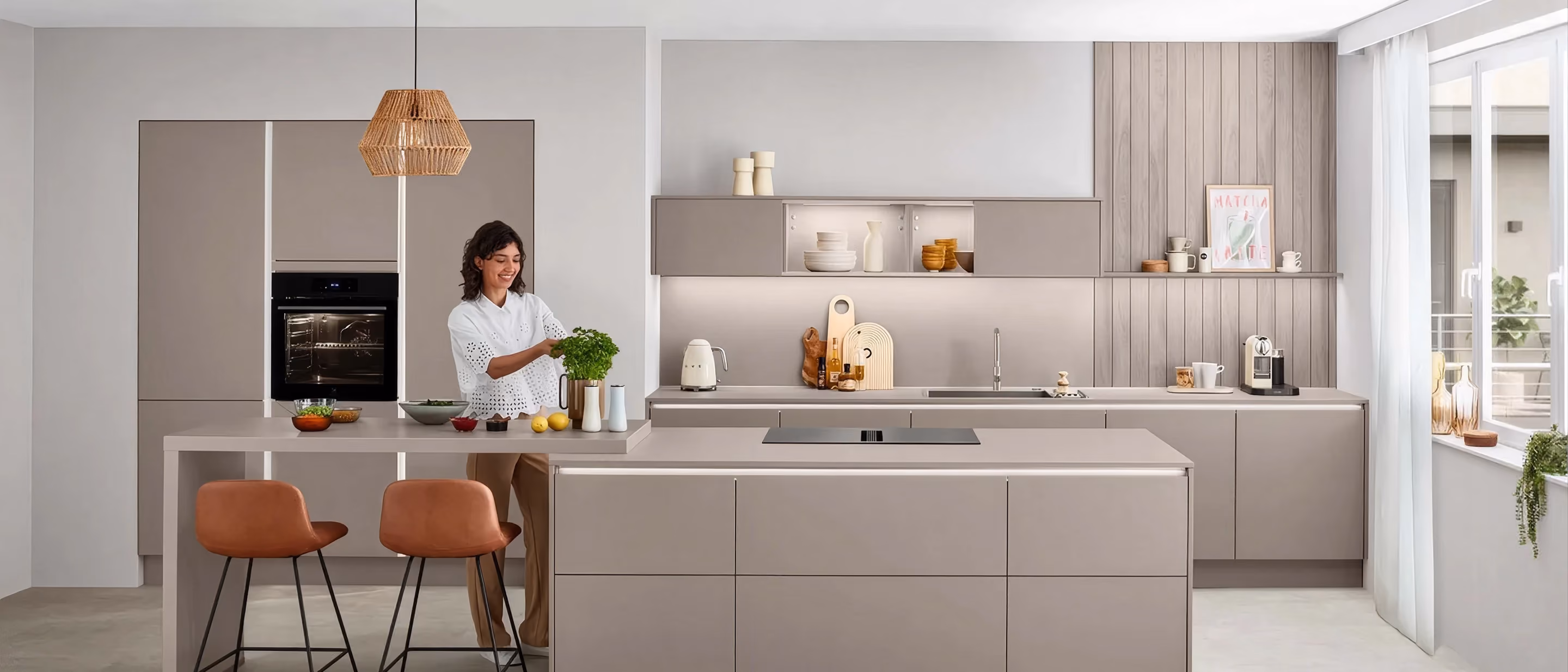 Moderne Küche in neutralen Tönen mit Kochinsel, integrierten Geräten und eleganter Beleuchtung, Person bereitet frische Kräuter vor.