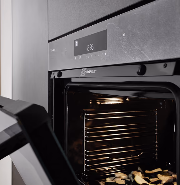 Geöffneter moderner Einbau-Backofen mit beleuchtetem Innenraum, in dem Gemüse auf dem Rost liegt.