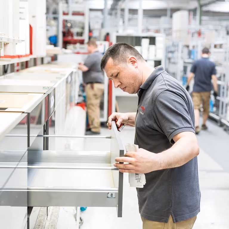 Ein Mann in grauem Poloshirt inspiziert in einer modernen Fabrikhalle einen geöffneten Schubladenschrank.