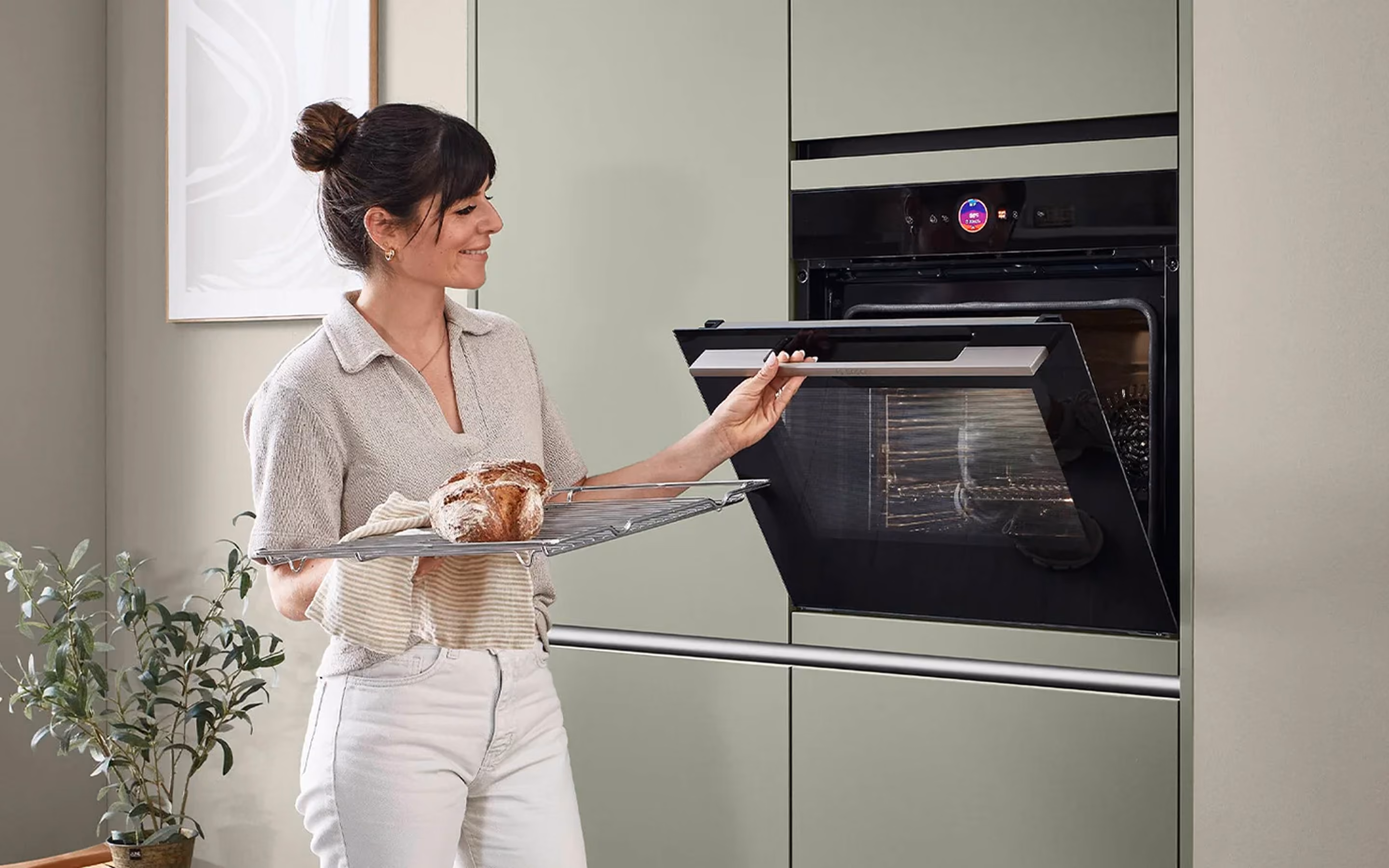Frau nimmt frisch gebackenes Brot aus einem eingebauten Ofen in einer modernen Küche mit grünen Schränken.