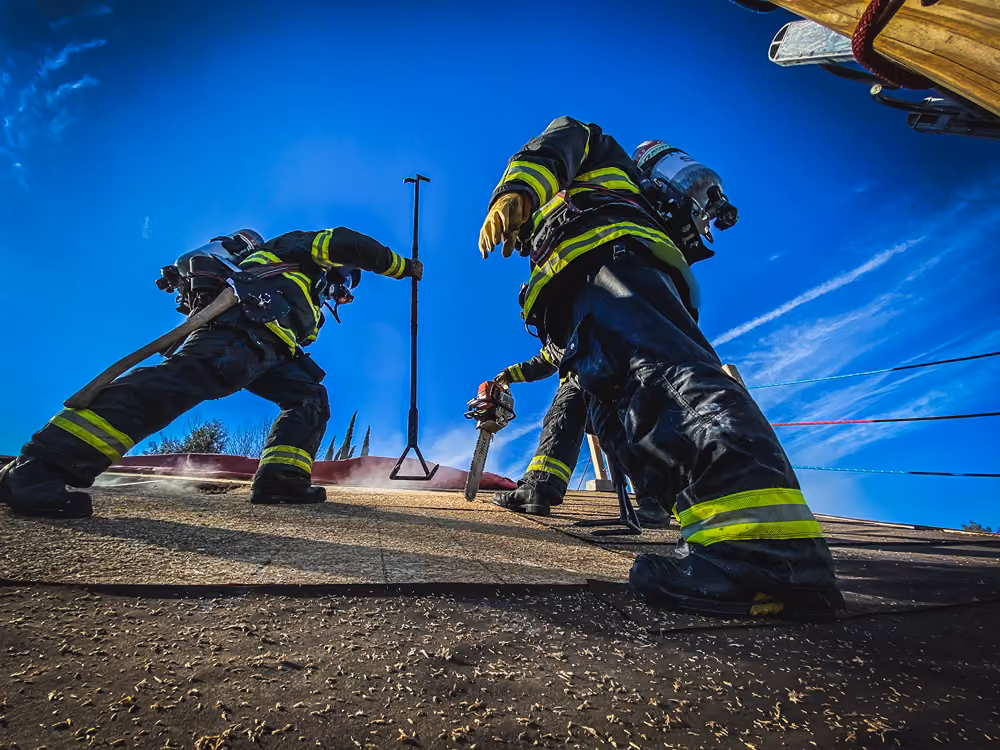 Firefighters on a rooftop using a chainsaw and pike pole during ventilation training