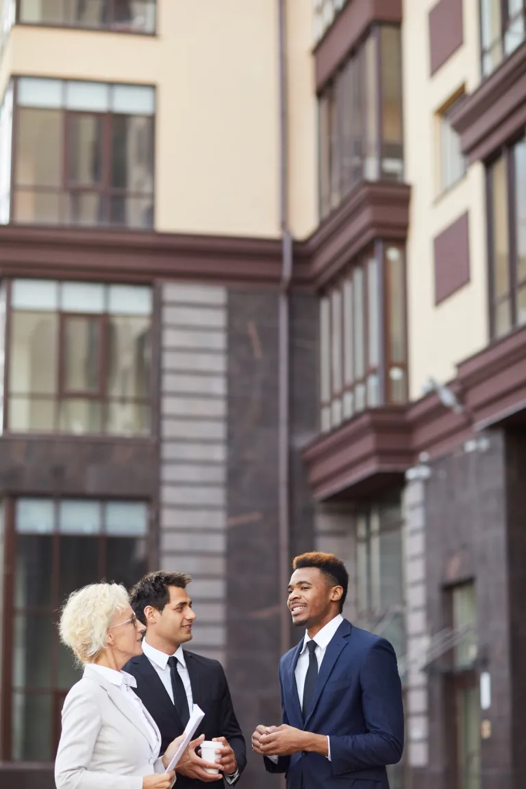 Three professionals engaged in discussion outdoors beside a building.