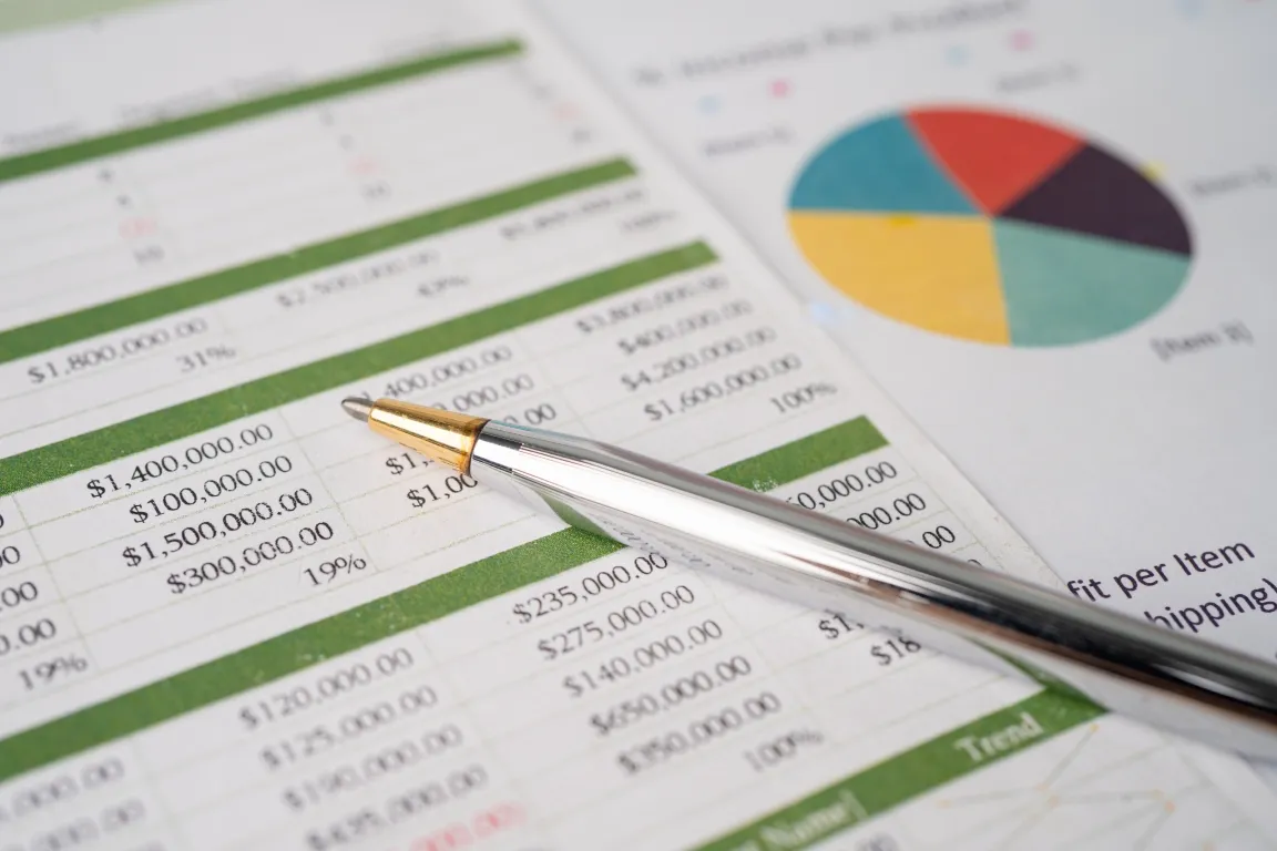 A pen resting on financial documents displaying numerical data and a pie chart.
